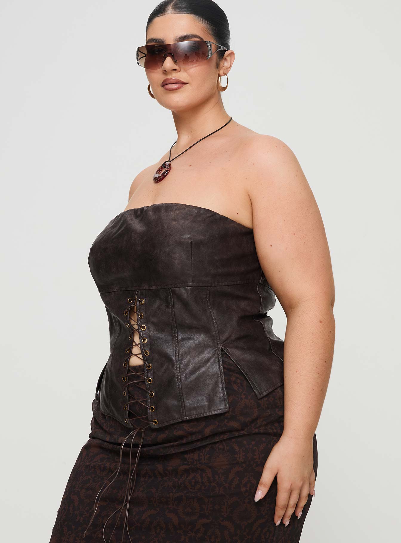 side view of model wearing Princess Polly Afraid Strapless Faux Leather Top Brown Curve Sleeveless straight 